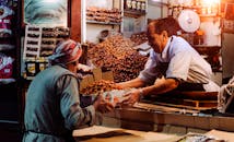 Two men exchanging dates in a vibrant Dubai spice market stall.